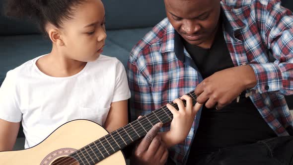 AfricanAmerican Man Teaching His Little Son to Play Guitar at Home