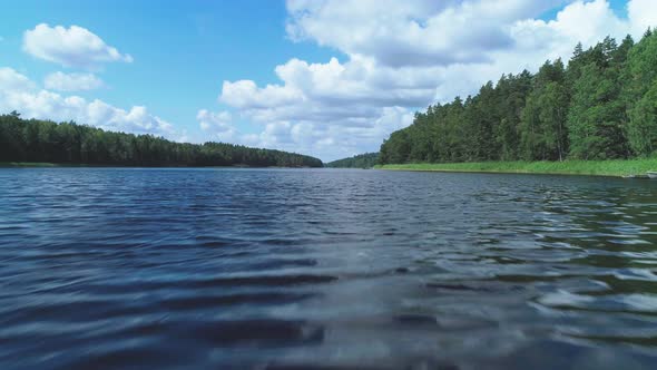 Aerial shot above a dark blue river in Sweden at daytime, surrounded with green forest and a blue sk