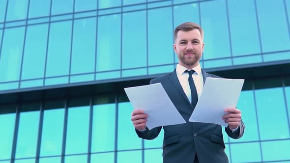 Portrait of a Confident Man in a Business Suit with Documents in Front of a Modern Office Building