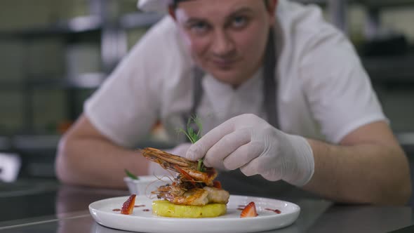 Closeup Plate with Delicious Seafood and Blurred Smiling Chef Decorating Dish with Greenery