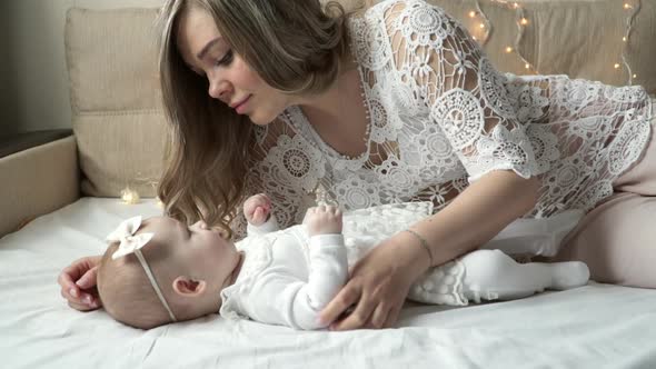 Young Mother Plays with Newborn Daughter Smiles and Kisses Little Hand of Baby