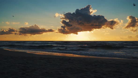 Sunset behind Clouds over Sea Waves and Sandy Beach