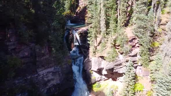 Aerial Through Two Waterfalls in Gorge Surrounded By Pine Trees