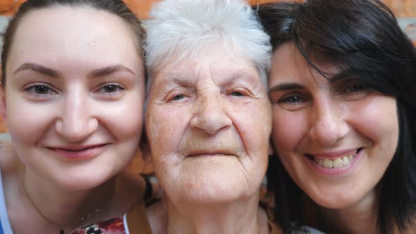 Portrait of Elderly Woman with Her Daughter and Granddaughter Looking Into Camera and Smiling