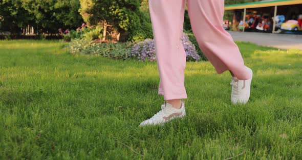 Female Legs in White Sneakers Going on a Grass