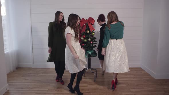 Group of young women in dresses dancing around christmas tree