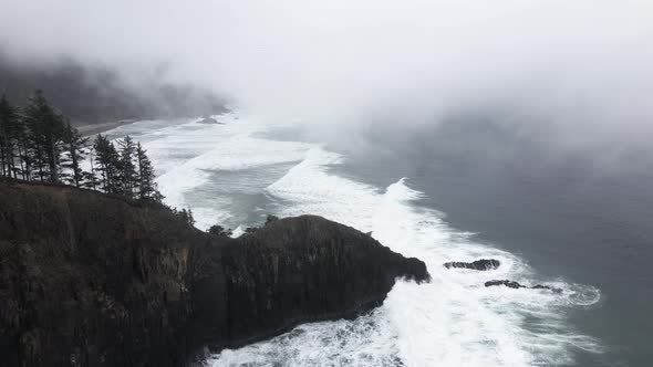 Descending on a fog shrouded tree lined ridge plunging into a jagged Oregon coastline, aerial