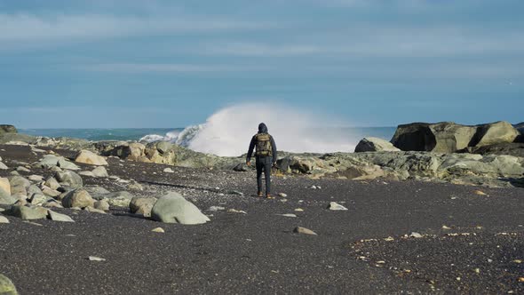 Man With Backpack On Black Sand Beach With Waves Crashing