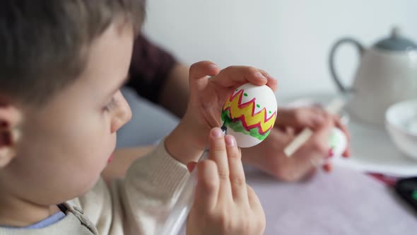 Little child draws patterns on an Easter egg