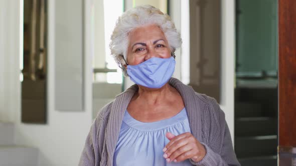 Portrait of african american senior woman wearing face mask opening front door and welcoming at home