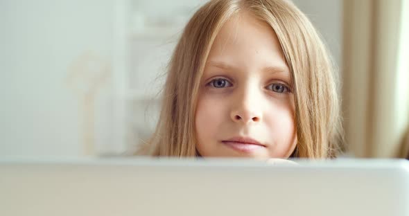 Portrait of Little Blonde Girl Sitting at Computer Laptop at Home or in Classroom, Child Looks at