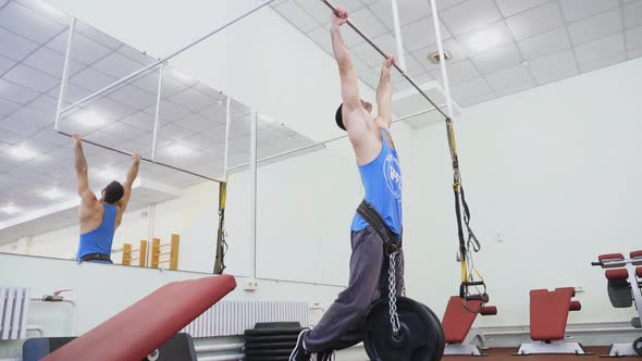 Muscular Sportsman Doing Pull Ups with Heavy Weight at Gym