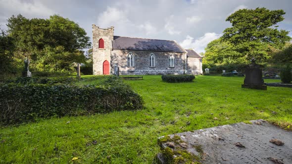 Time lapse of rural graveyard with church in background in Ireland during a cloudy day with rainbow