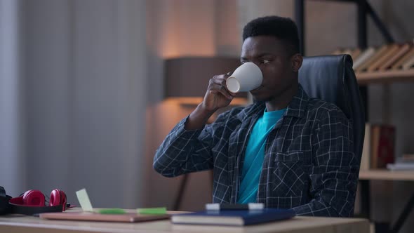 Portrait of Satisfied Young Handsome African American Man Drinking Tea or Coffee in Living Room