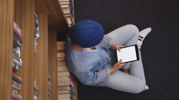 Asian female student wearing a blue hijab sitting on the floor and using tablet