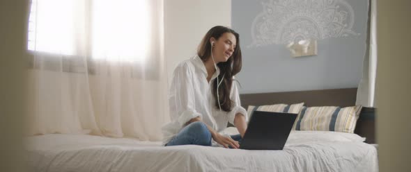 A young woman speaking to someone through earphones while working on her laptop