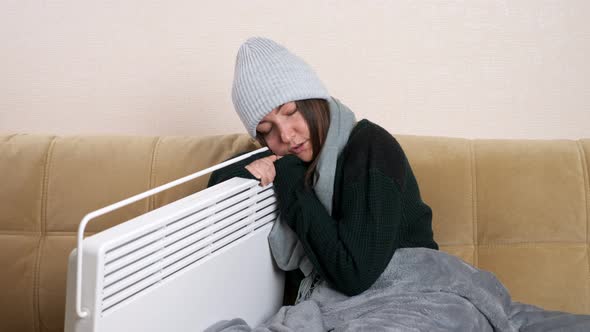 Young Woman Hugs Heater Sitting on Sofa in Living Room