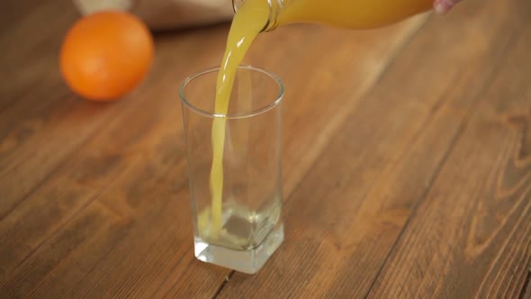 Orange Juice is Poured Into a Glass Standing on a Wooden Table