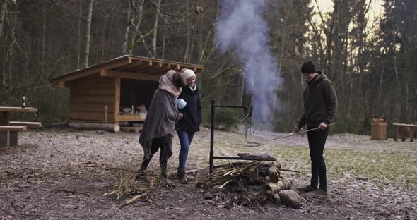 Camping Friends Stand Around The Campfire While Cooking Food.