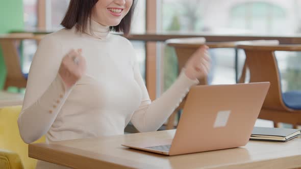 Unrecognizable Satisfied Young Woman Making Victory Gesture and Smiling Sitting in Cafe with Laptop