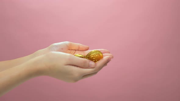 Golden bitcoin digital currency drop on hand, isolated on pink background.