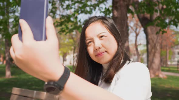 Close up Asian woman sitting on a chair at a park and using her smartphone to take a selfies