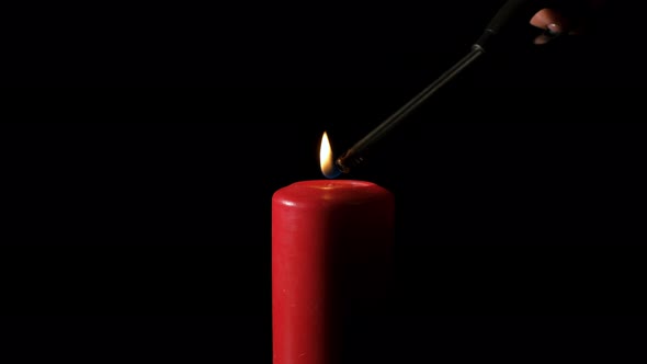 A Woman Lights a Red Candle in a Dark Space.