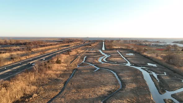 An aerial view over a marsh on Long Island, NY. A long road with a few cars run next to it, shot on