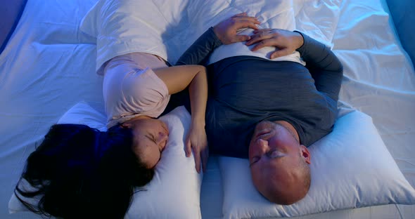 A Married Couple: a Bald Man and a Dark-haired Woman Are Lying on a Bed on White Bed Linen