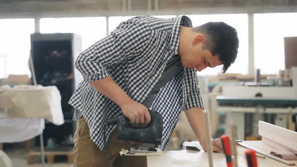 Young Carpenter Using Jigsaw Power Instrument To Saw Wood in Workshop