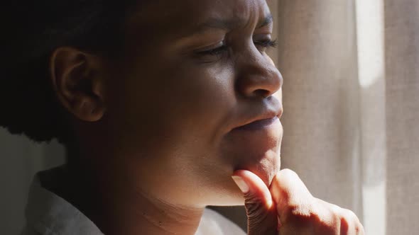 Thoughtful african american woman looking through window in bedroom