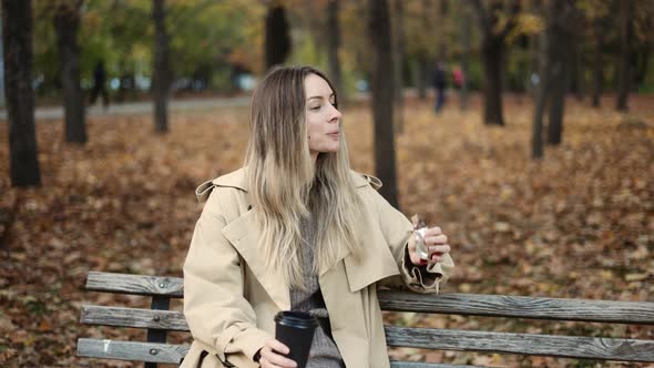 Woman Drinking Take Away Coffee and Eat Chocolate in Autumn Park