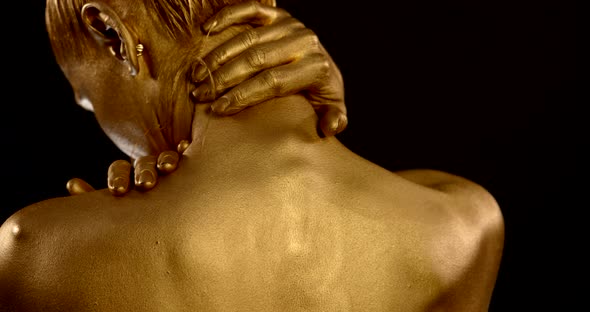Close-up of a Woman's Back with Golden Glowing Skin on a Black Background. the Girl Strokes Her Neck