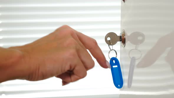 Steel Key with Blue Keyholder in Metal Door Lock. Female Hand Touching Keyholder with Finger To Make