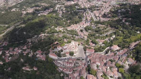 The Palace of Sintra surrounded by picturesque houses and Natural Park forest. Circling aerial view