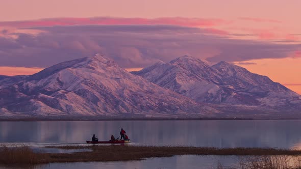 People in canoes during sunset on Utah lake against snow capped mountains