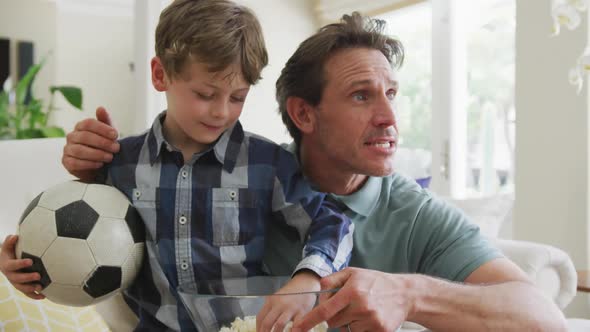 Happy caucasian father and son watching tv and supporting in living room