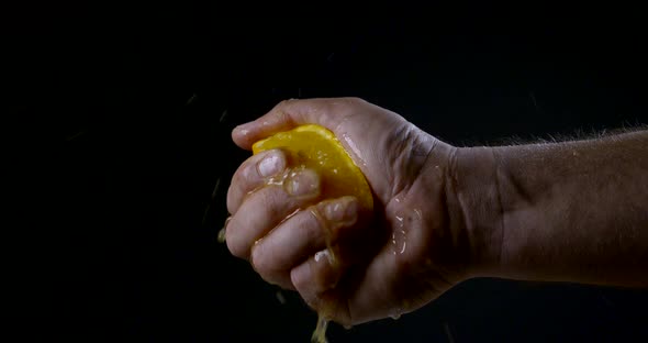 Close-up Hand on a Black Background Squeezes Citrus Fruit - Orange, Lemon. Slow Motion.