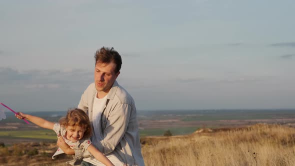 Family Vacation In Nature. Dad Holds Little Daughter And His Son Runs Around. Man Twists His