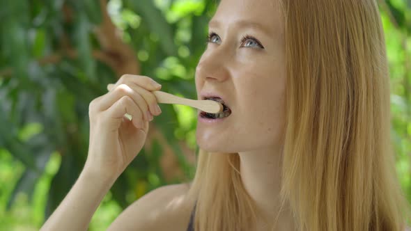 A Young Woman in a Green Environment Brushes Her Teeth with a Black Active Charcoal Powder for Teeth