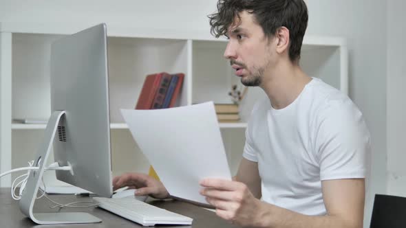 Young Creative Man Reading Documents and Working On Desktop alt