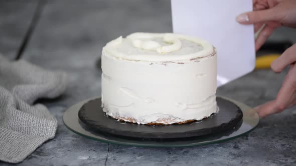 Confectioner Woman is Smearing Cream on Sides of Cake Using Spatula Closeup View