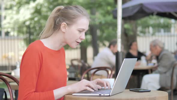 Young Woman Celebrating on Laptop Sitting in Cafe Terrace
