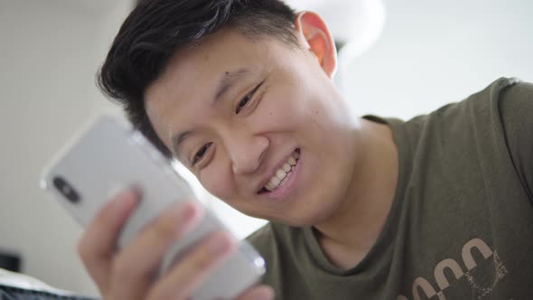 A Young Asian Man Works on a Smartphone and Smiles  Closeup From Below