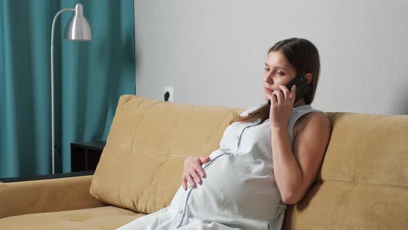 Pregnant Woman Talking on the Phone Experiencing Contractions While Sitting on the Couch