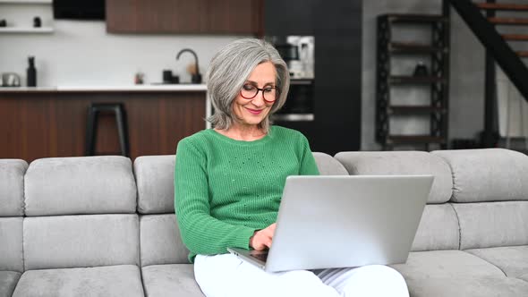 Mature Senior Woman Is Using a Laptop at Home