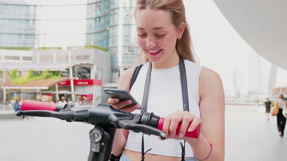 Slow motion young woman using smartphone scaning qr code unlocking kick scooter