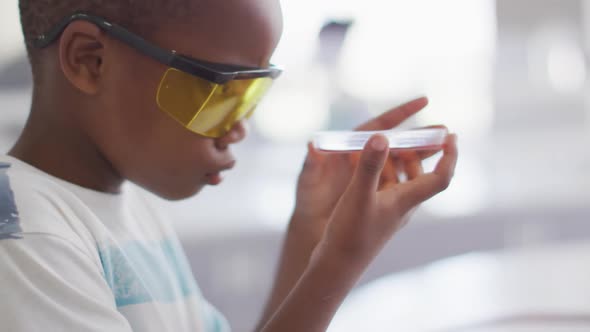 Video of happy african american boy wearing glasses and holding reagent during chemistry lesson