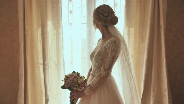 Beautiful Blonde Bride Holds Flower Bouquet Near the Window