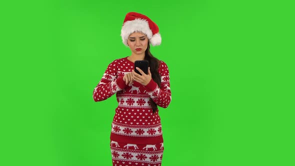 Sweety Girl in Santa Claus Hat Is Angrily Texting on Her Phone. Green Screen